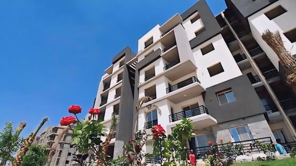 a building with red flowers in front of it at Stylish Flat at Jannah Compound Sheikh Zayed in Sheikh Zayed