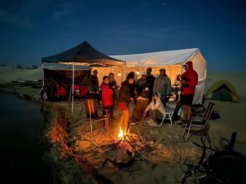 a group of people standing around a fire in a tent at Avistamiento de Ballenas y Campamento Todo incluido!! Mínimo 3 noches en Mag Bay in Punta Cove