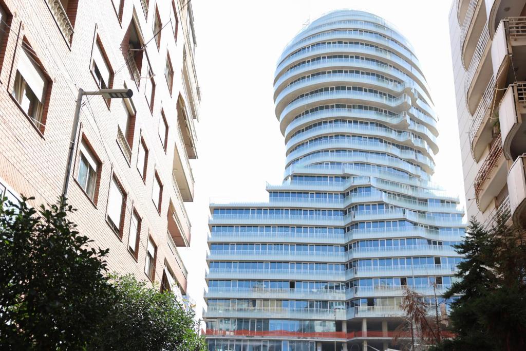 a tall glass building in the middle of two buildings at The Central Spot in Tirana