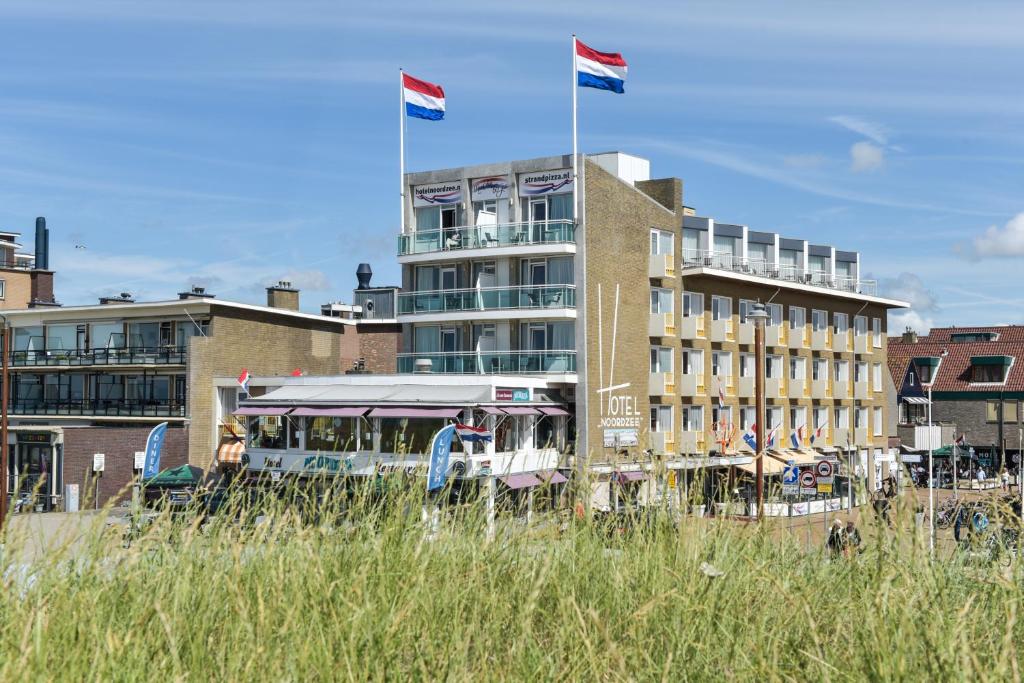 ein Bus, der vor einem Gebäude mit zwei Flaggen parkt in der Unterkunft Hotel Noordzee in Katwijk
