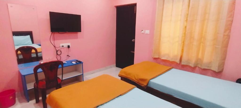 a room with two beds and a desk and a tv at Nirmal Guest House in Marakkānam