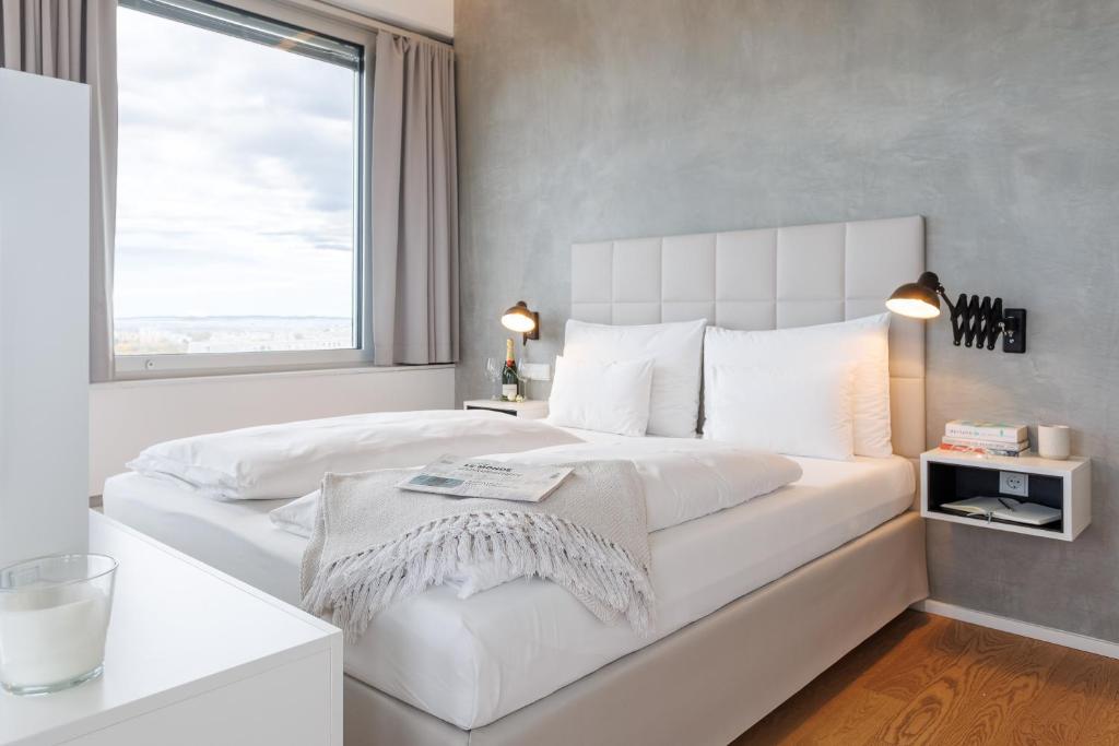 a white bedroom with a large bed with a window at Exklusives Skyline-View Loft - Nähe Zentrum Wien in Vienna