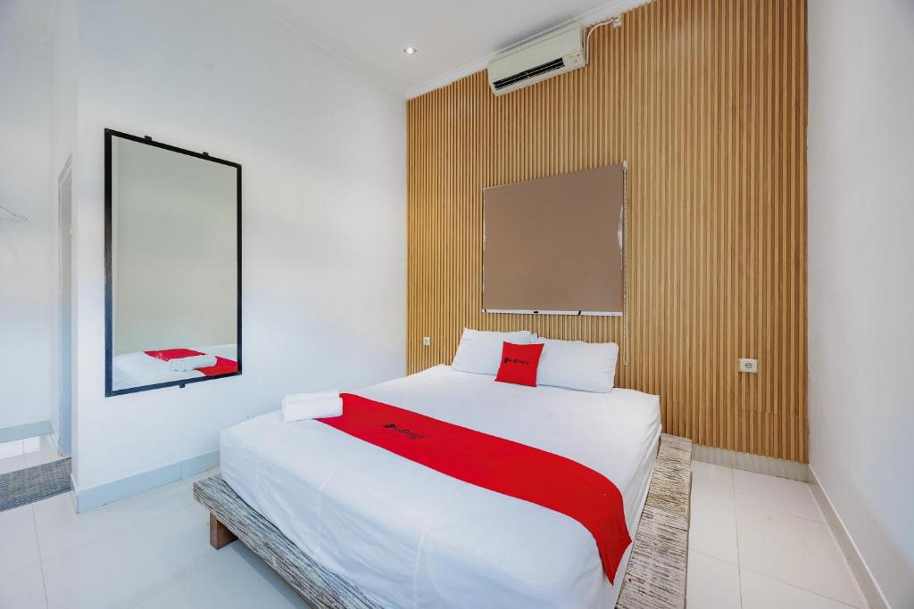Un dormitorio con una gran cama blanca con una manta roja. en RedDoorz near Ubud Village, en Sukawati