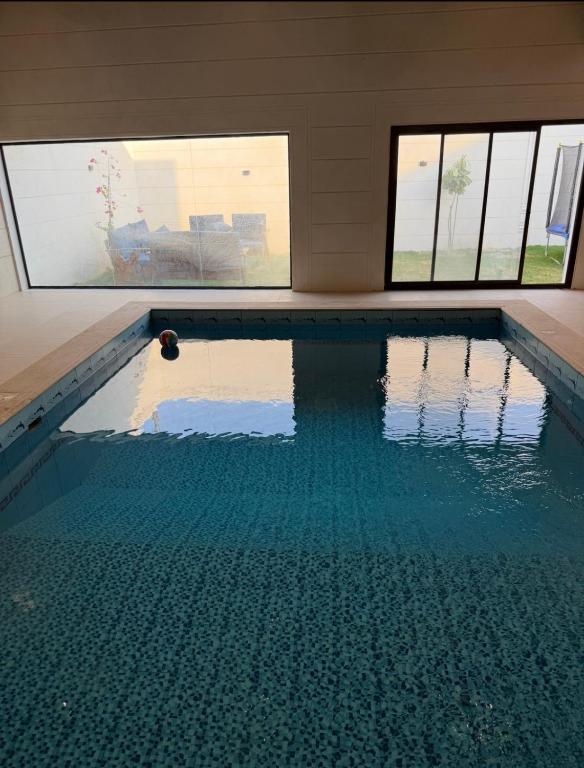 Una piscina con agua azul en una habitación con ventanas. en شاليه داله العماريه1 بالكامل لك وأجواء ممتعه, en Abā al Kibāsh