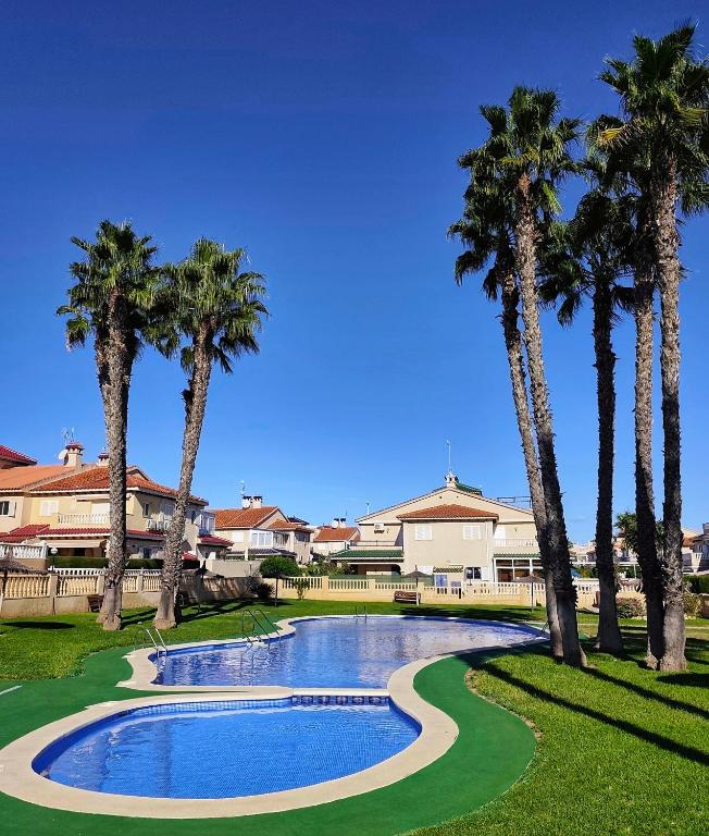 a swimming pool with palm trees in front of a house at Light Blue Apartment Orihuela Costa in Orihuela Costa