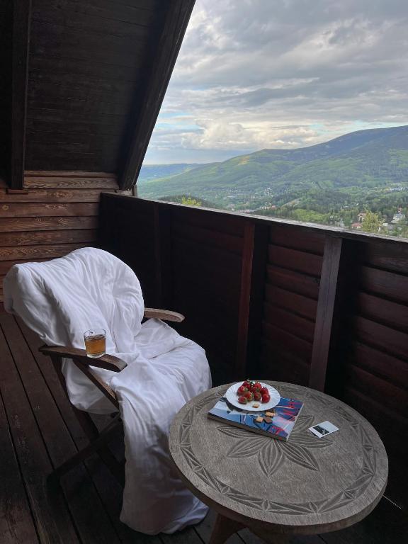 Wooden balcony chair draped in white cover beside table with strawberries and drink, mountain vista.