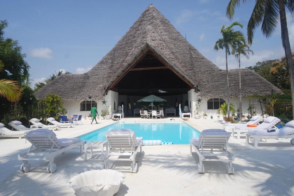 Un complejo turístico con piscina, tumbonas y techo de paja. en Lilys Haven, en Malindi