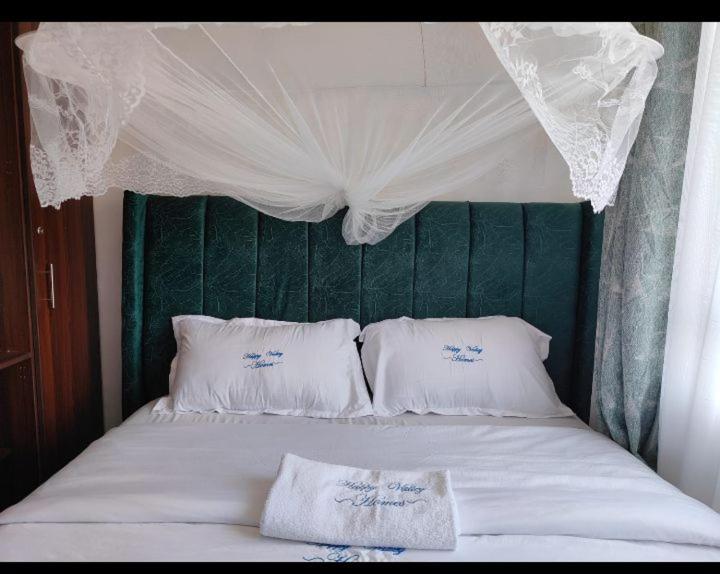 a bed with a green headboard and white pillows at Happy Homes BnB in Kisumu
