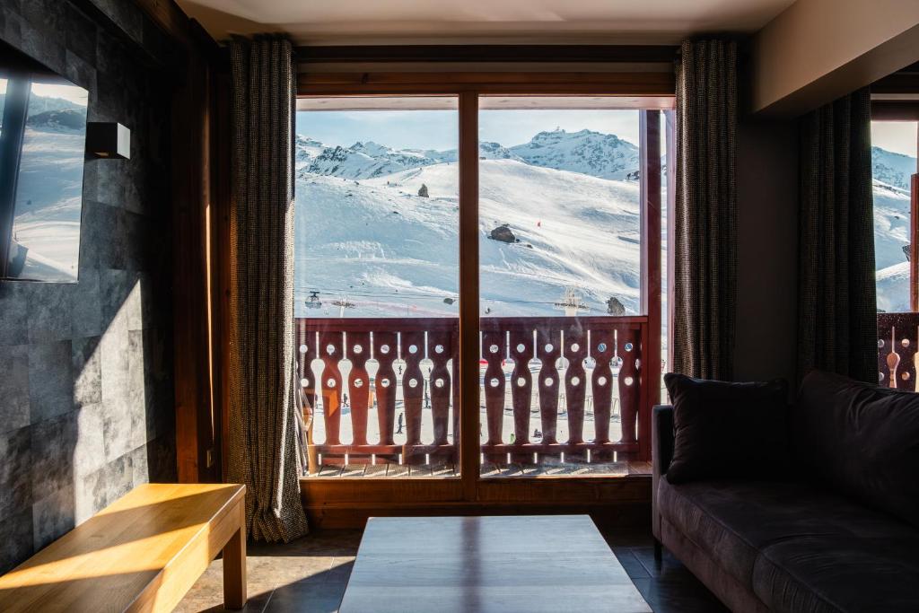 a living room with a view of a snowy mountain from a window at Résidence Montana Caron by Village Montana in Val Thorens