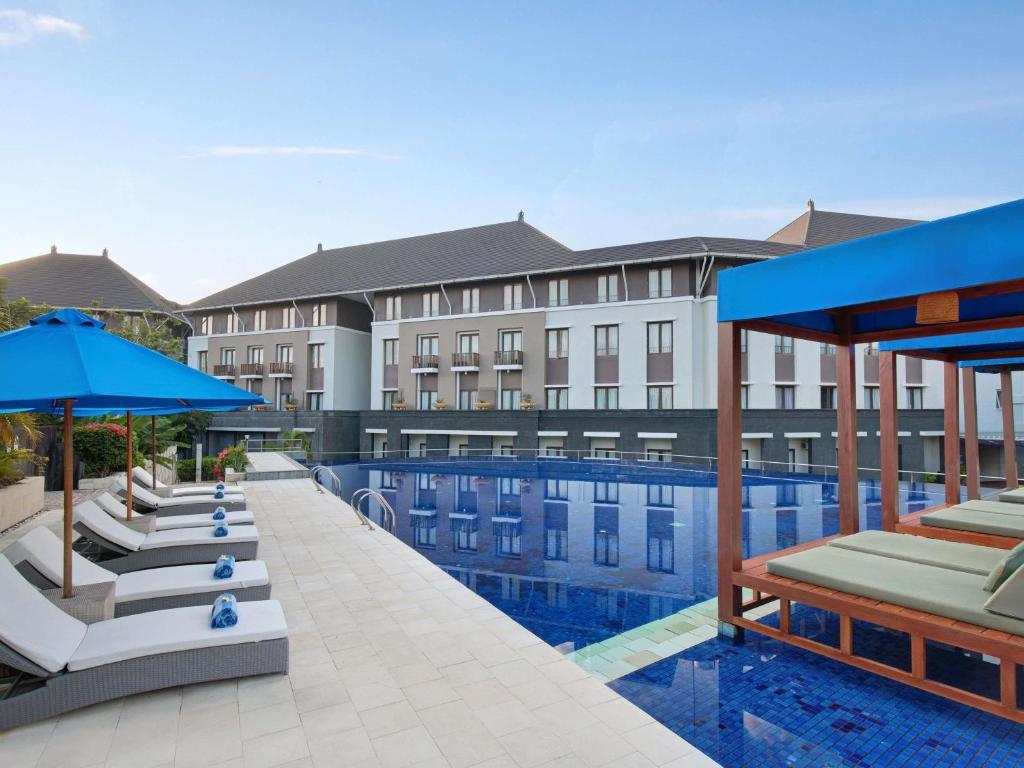 a hotel pool with lounge chairs and umbrellas at Mercure Bali Nusa Dua in Nusa Dua