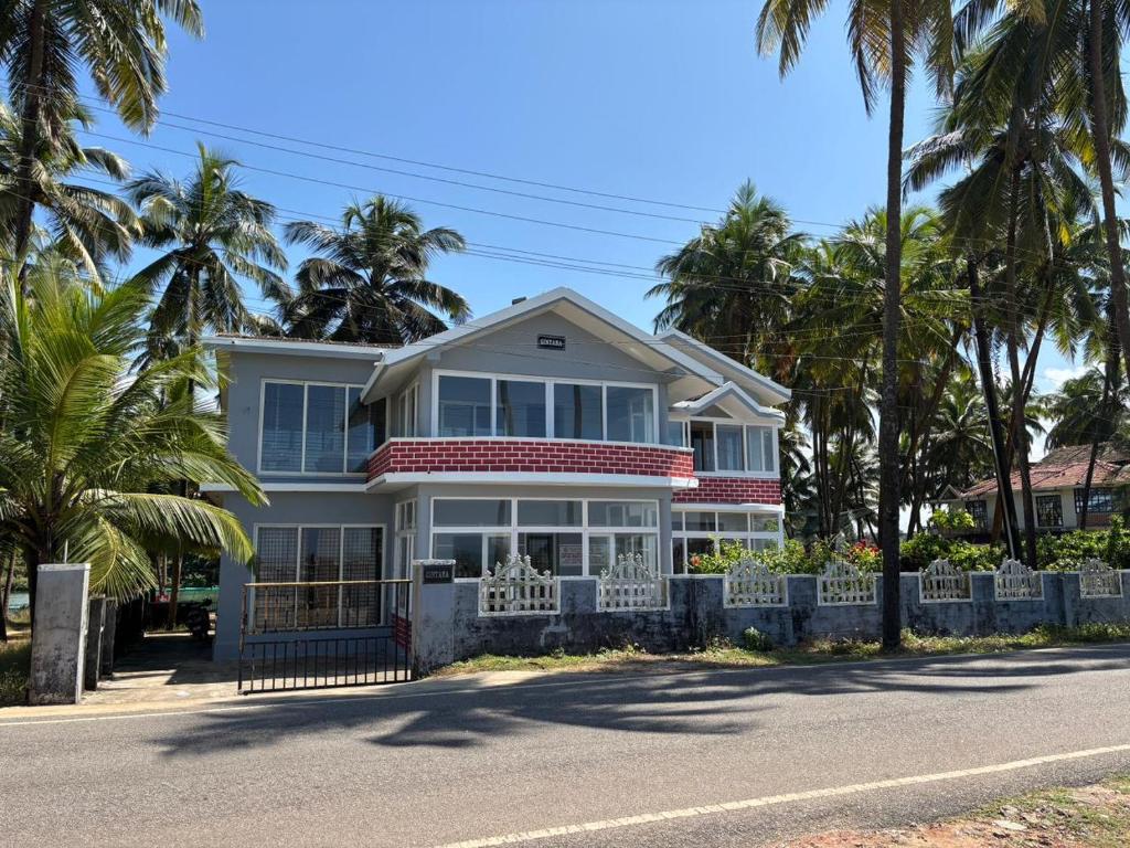 a white house with palm trees on the street at Gintara Beach Homestay by evaddo in Kalyānpur