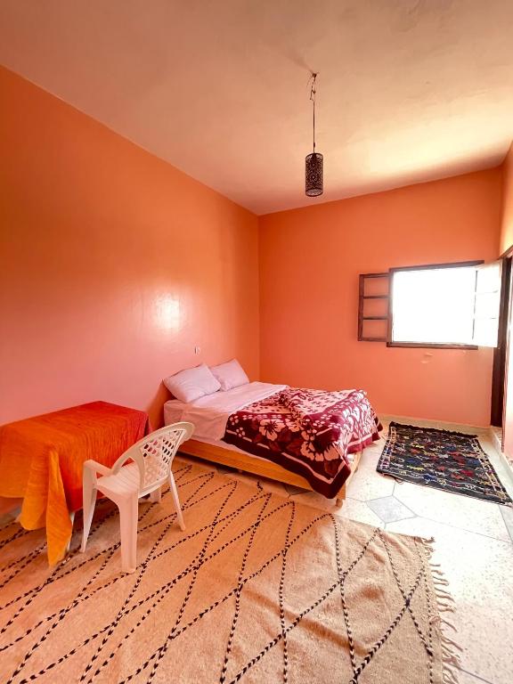 1 dormitorio con paredes de color naranja, 1 cama y 1 silla en Hostel merzouga, en Merzouga