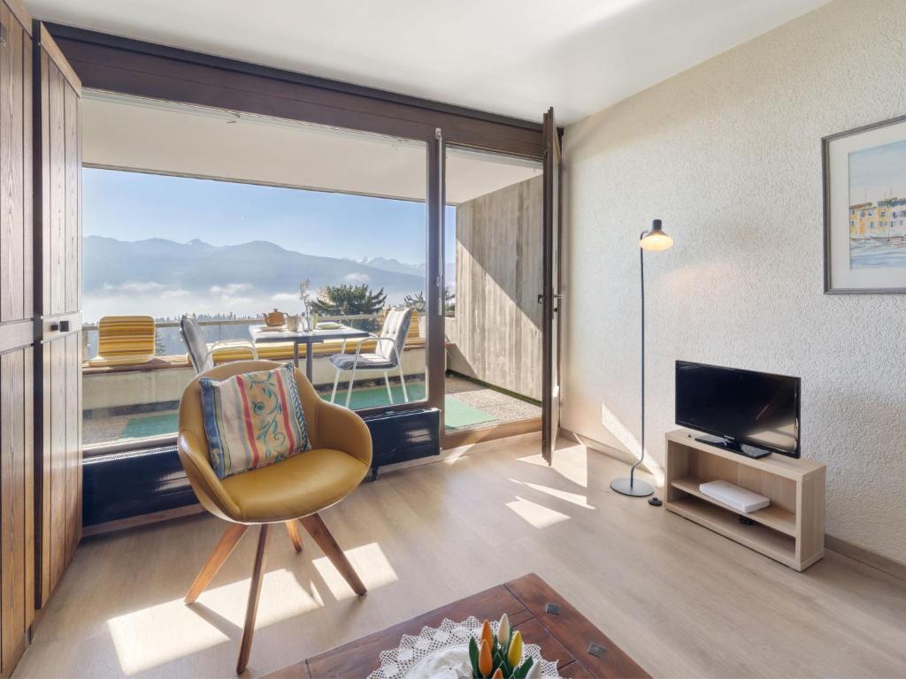 a living room with a chair and a television and a balcony at Studio Jeanne D'Arc Apt- A-8 by Interhome in Crans-Montana
