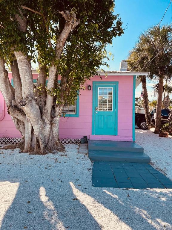 a pink house with a blue door and trees at Playa Esmeralda Cottage! Add Golf Cart!! in Bradenton Beach