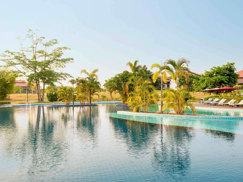 a large swimming pool with palm trees and water at The Lake Garden Hotel Nay Pyi Taw - MGallery Collection in Nay Pyi Taw