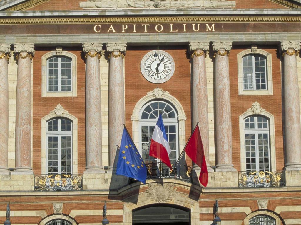 drie vlaggen voor een gebouw met een klok bij hotelF1 Toulouse Aéroport in Blagnac