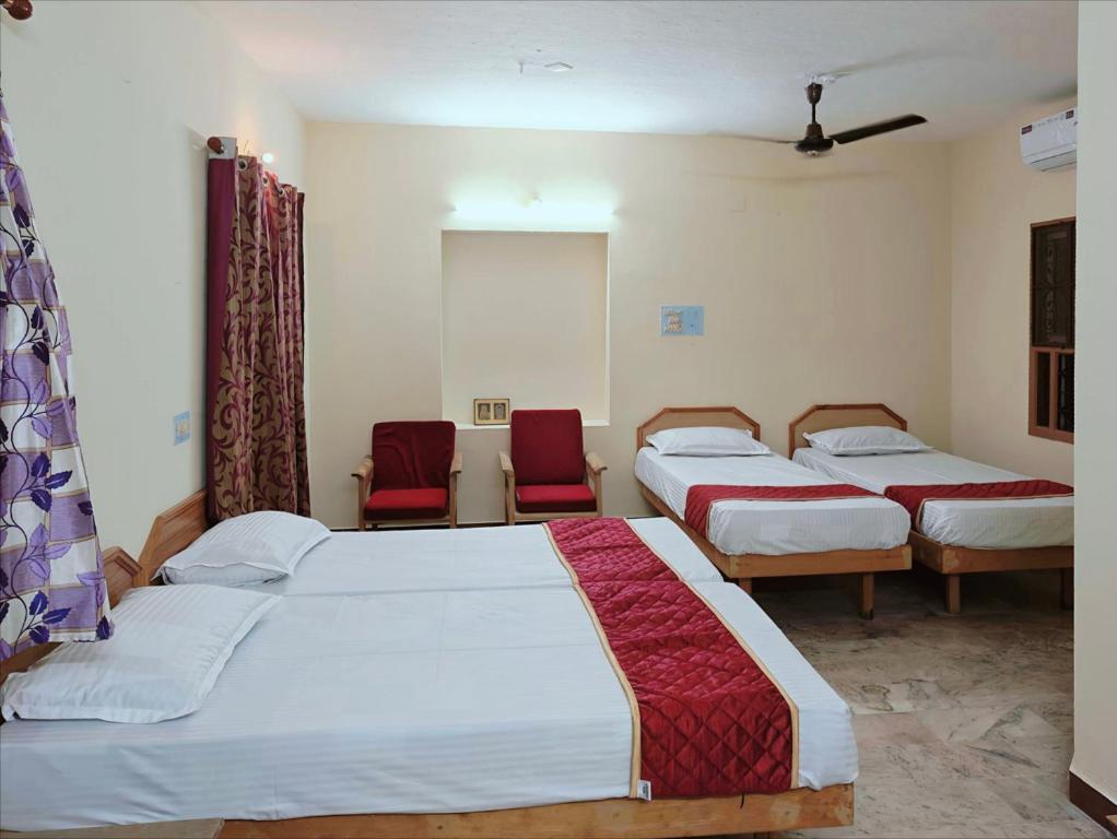 two beds in a room with two red chairs at Daya Dharmam Residency in Tiruvannāmalai