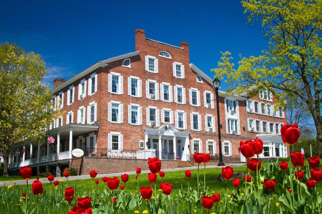 un grand bâtiment en briques avec des fleurs rouges devant lui dans l'établissement Middlebury Inn, à Middlebury