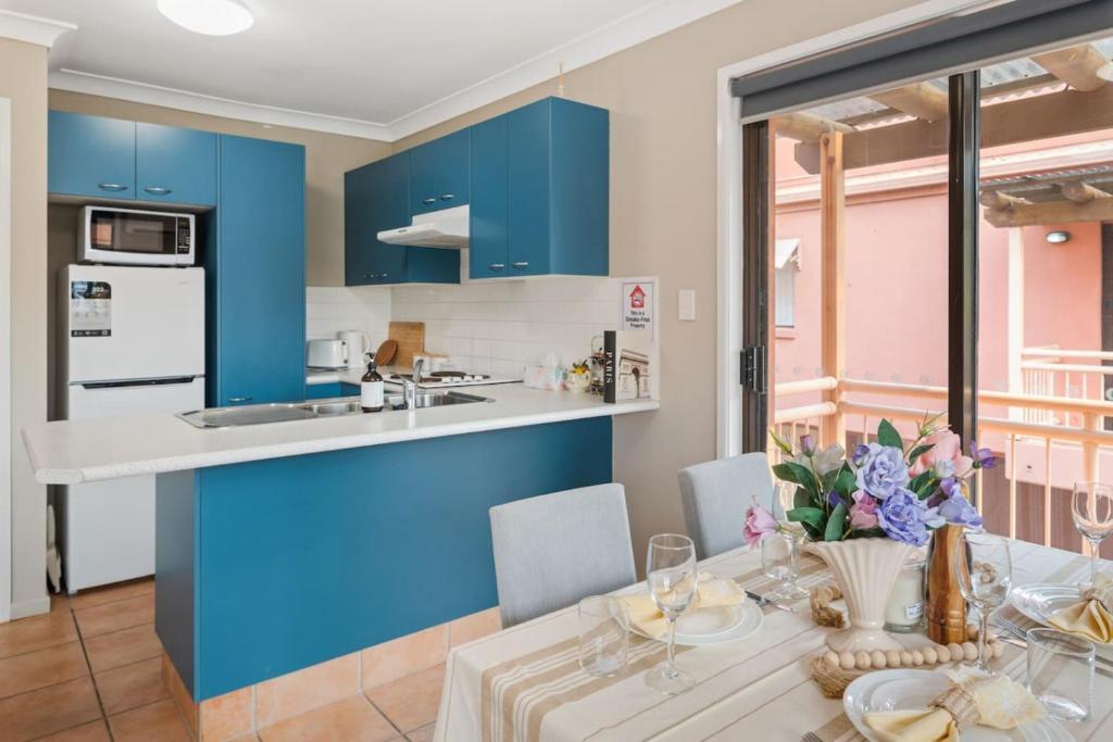 Modern 2BR Apartment Beach and Dining in Broadbeach في غولد كوست: مطبخ وغرفة طعام مع دواليب زرقاء وطاولة