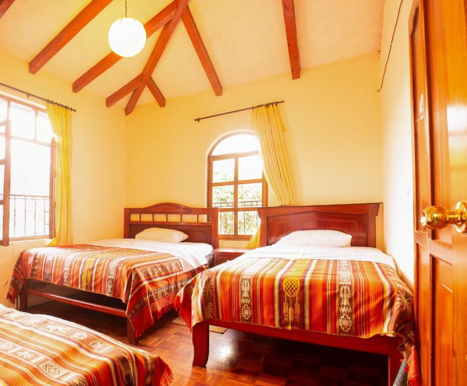 a bedroom with two beds and two windows at Casa del Huesped in Otavalo