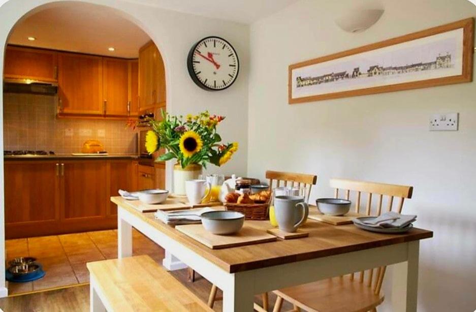 a kitchen with a table and a clock on the wall at Nikolaus Cottage Cotswolds in Winchcombe