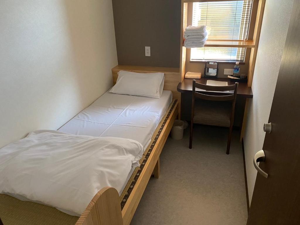 a small room with a bed and a desk with a chair at 八戸駅西口民泊ゲストルームNvillage in Hachinohe