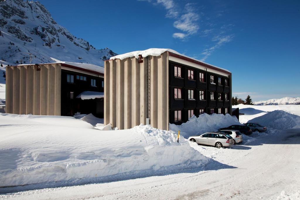 un bâtiment recouvert de neige avec des voitures garées devant dans l'établissement Residence Savoia, à Passo del Tonale