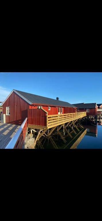 a red building with a wooden bridge next to the water at Stinebua in Vestvågøya