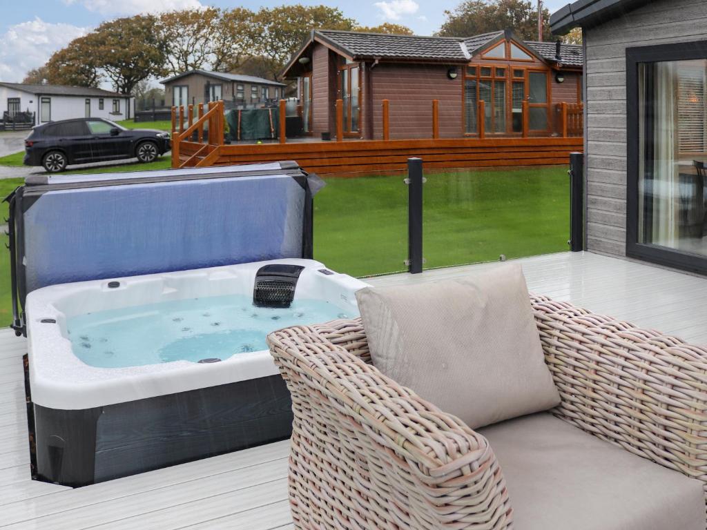a hot tub on a patio with a wicker chair at 38 At The Sanctuary Lodges - Uk50850 in Carnguwch