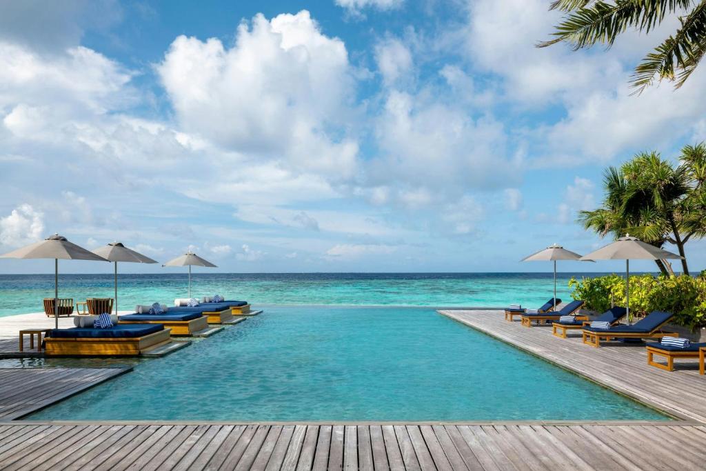 a pool with chairs and umbrellas next to the ocean at The Halcyon Private Isles Maldives, Autograph Collection in Gaafu Alifu Atoll