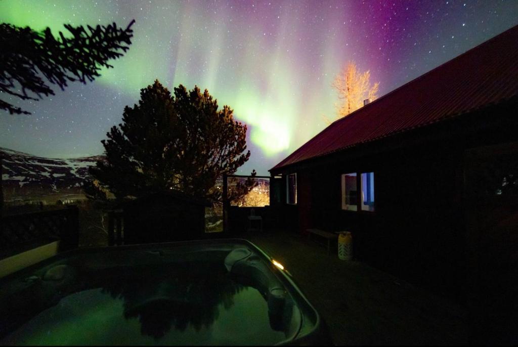 a view of the northern lights in the sky over a house at Cheerful forest cabin Fireplace and Hot tub in Akranes