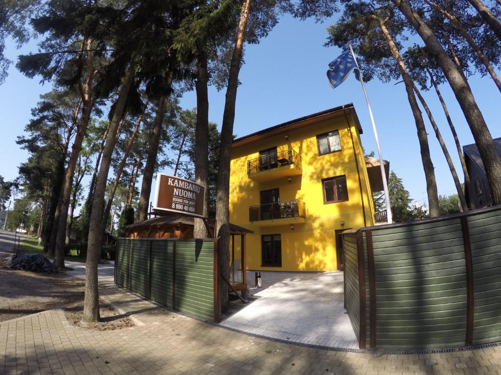 ein gelbes Gebäude mit einem Zaun und Bäumen in der Unterkunft Kambarių nuoma Kačerginės kurorte in Kačerginė