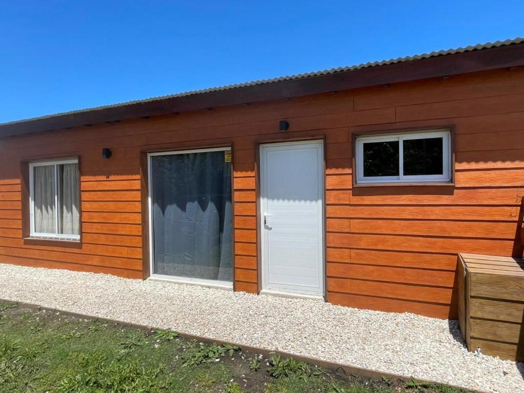 a wooden house with a white door and two windows at Cabaña Zona Las Brusquitas in Miramar
