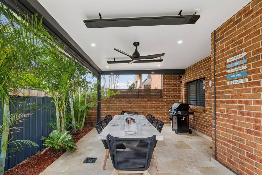 a patio with a table and chairs and a brick wall at Coledale Beach Escape - Modern Comfort by the Sea in Coledale
