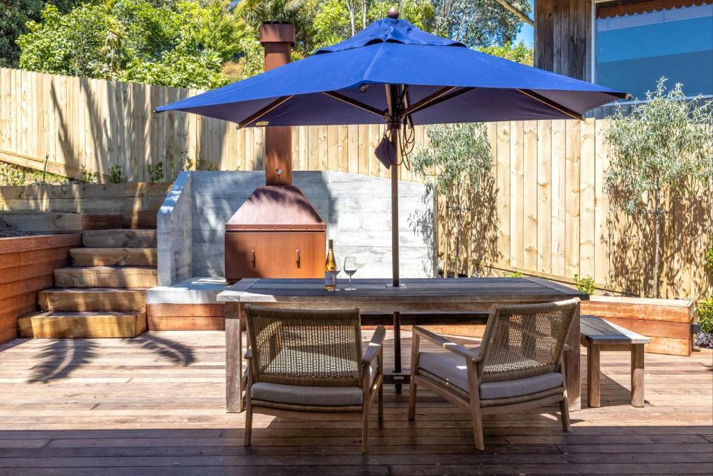 a wooden table with a blue umbrella on a patio at Bay Haven - Walk to Palm Beach in Waiheke Island