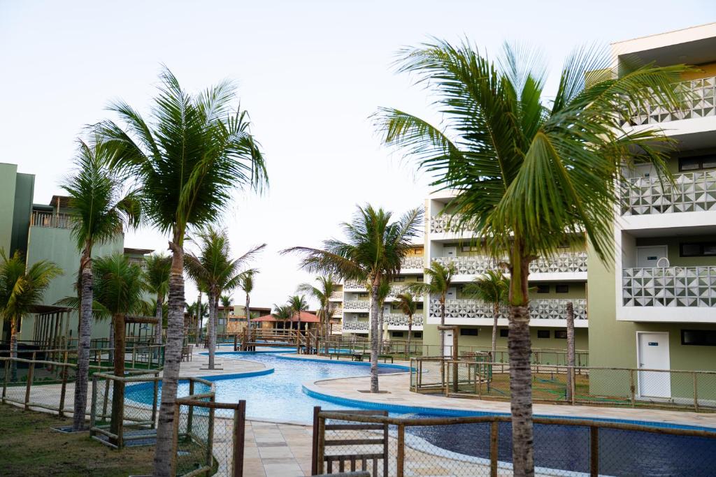 a swimming pool with palm trees in front of a building at Oásis Vistamar in Luis Correia