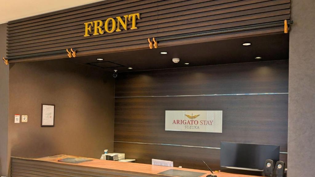 Un mostrador de recepción de un hotel Aragonasystay con un cartel en la pared en Arigato Stay Suzaka, en Suzuka