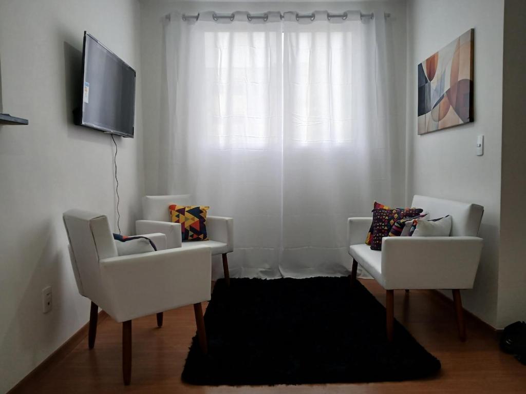 a living room with two white chairs and a television at Apartamento com piscina e garagem privativa in Londrina