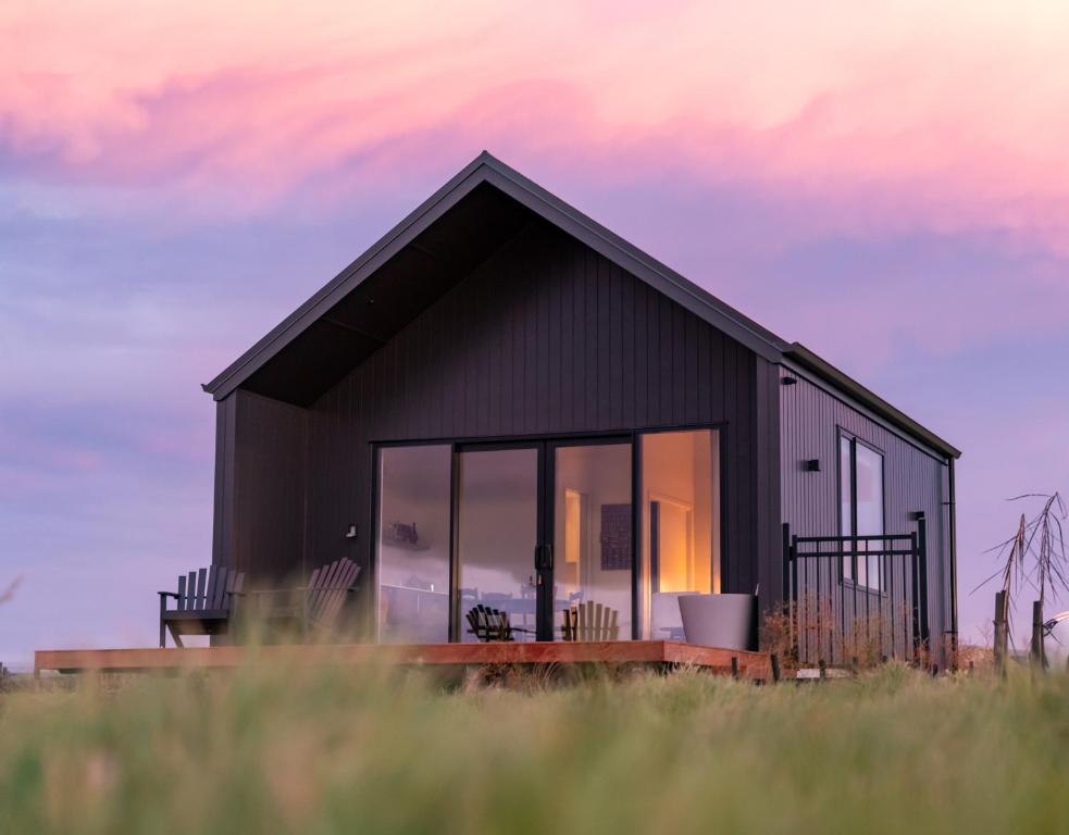 a black house with large windows on a field at Harvest Rise Vineyard Cottage in Pahautea