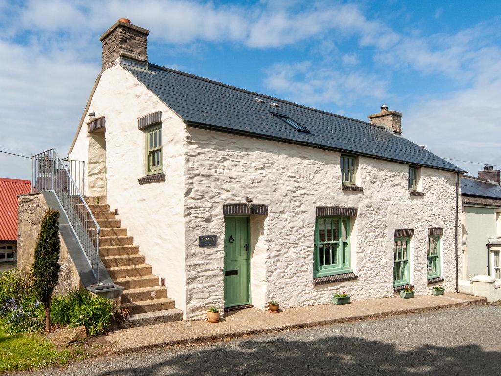 a white stone house with a green door and stairs at Ty Menyn in Mathry