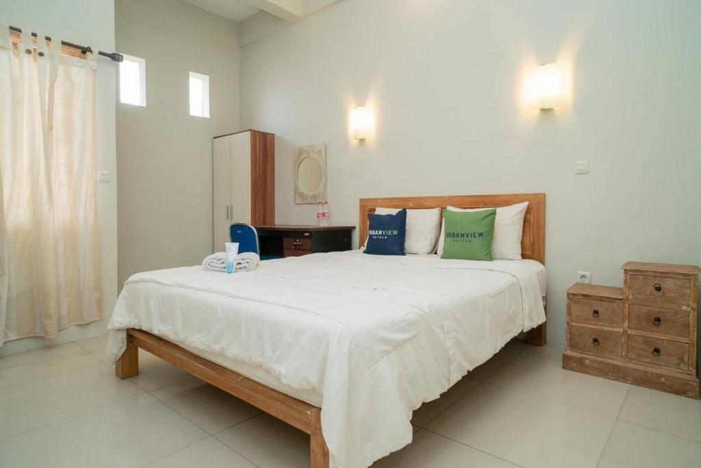 a bedroom with a large white bed with blue and green pillows at Urbanview Hotel Wayan Mansion in Denpasar