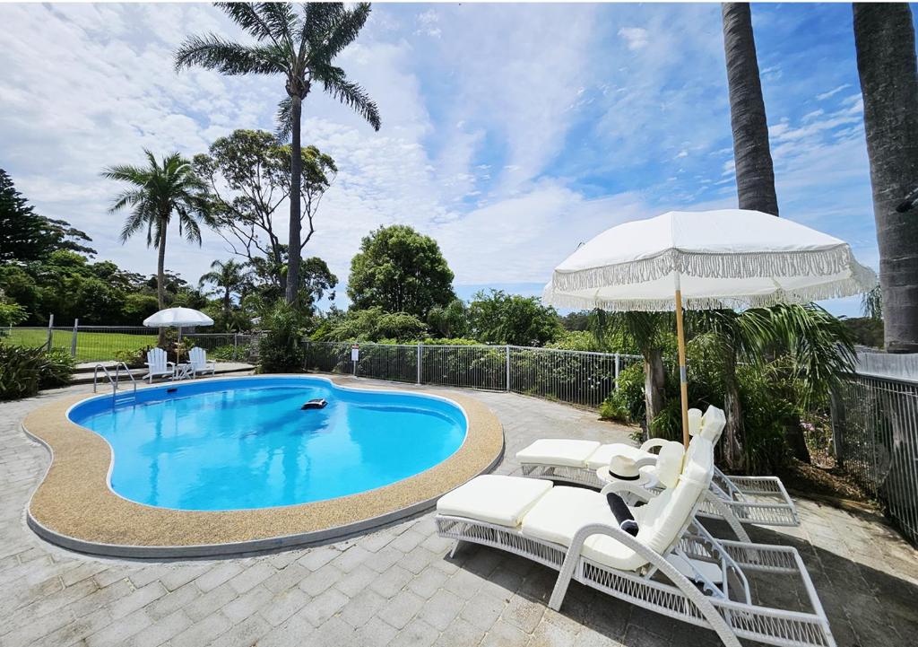 a swimming pool with two lounge chairs and an umbrella at Mollymook Ocean View Motel - Welcoming Guests 18 Years and Older in Mollymook