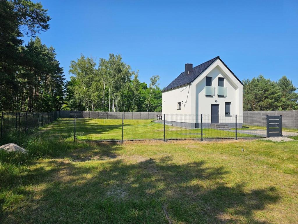 a white house in a field with a fence at Leśny Zakątek Świączyń 