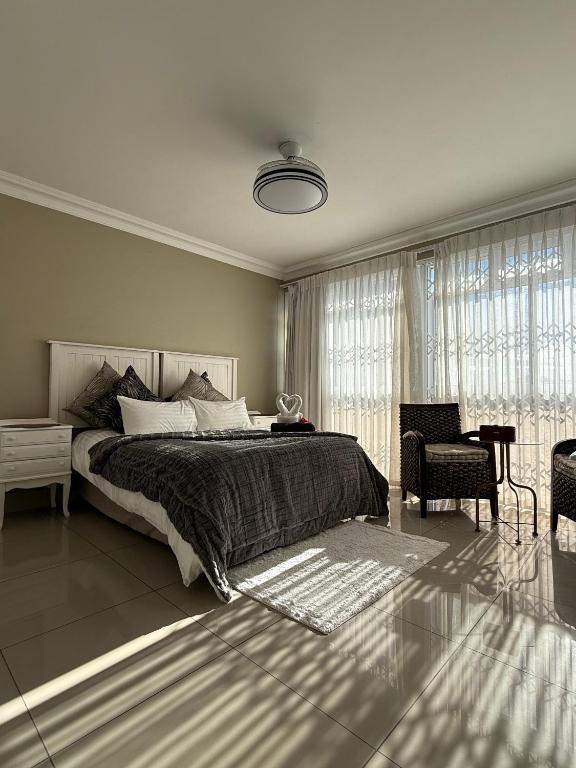a bedroom with a bed and a chair and windows at The Ocean Nook - Modern Beach Condo in Gqeberha