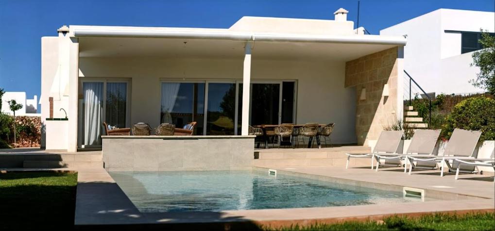 a house with a swimming pool and some chairs at VILLA PETRA ARENAL D'en CASTELL in Es Mercadal