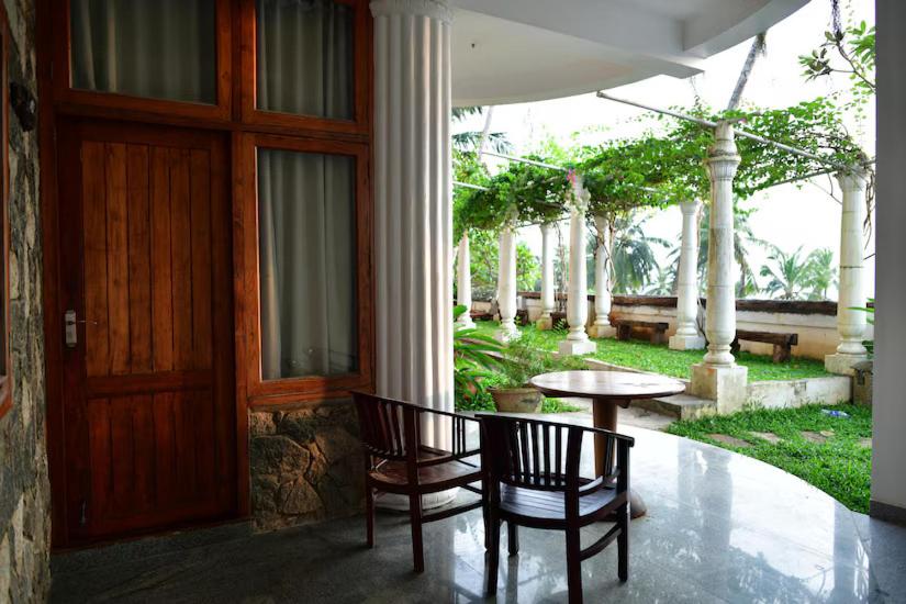 een veranda met 2 stoelen, een tafel en een deur bij By The Bay Kovalam in Trivandrum
