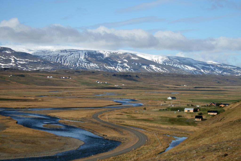 a winding river in a field with snow covered mountains at Dæli Apartments in Víðidalstunga