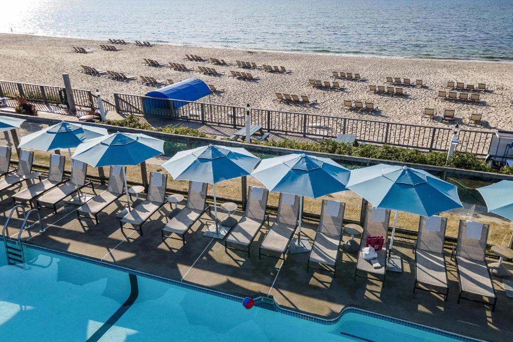 a swimming pool next to a beach with chairs and umbrellas at Blue Water Resort in South Yarmouth