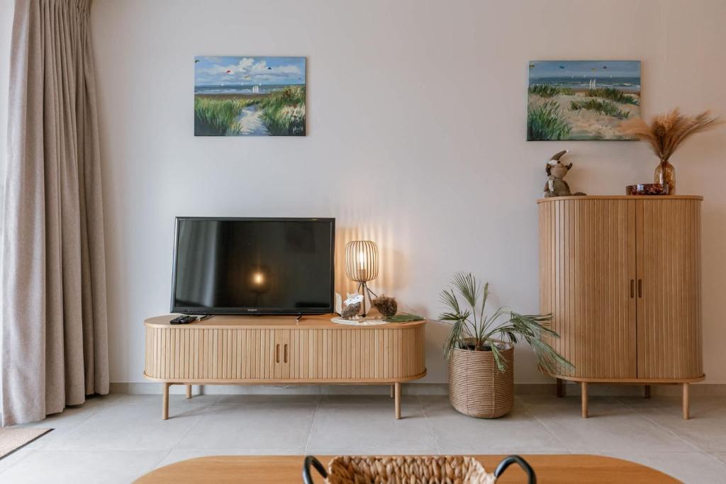 a living room with a flat screen tv on a wooden cabinet at Balcony Beach & Pool Access Family-Friendly Stay in Nieuwpoort