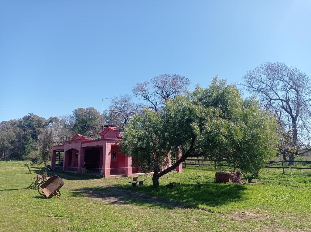 een rood huis in een veld met een boom bij La Chacra in Pilar